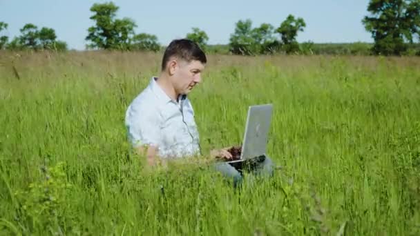 Uomo d'affari lavora dietro un computer portatile seduto sull'erba — Video Stock