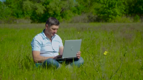 Бизнесмен работает за ноутбуком, сидя на траве — стоковое видео