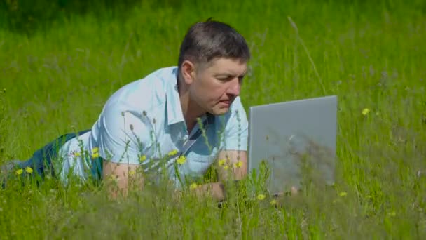 Бизнесмен работает за ноутбуком, лежащим на траве — стоковое видео