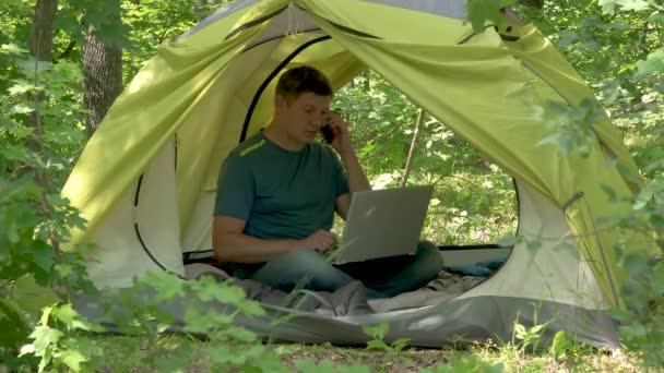Üzletember Laptopin mögött dolgozik egy sátorban az erdőben. — Stock videók