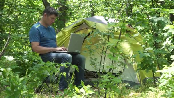 Üzletember Laptopin mögött dolgozik, közel az erdő sátrához. — Stock videók