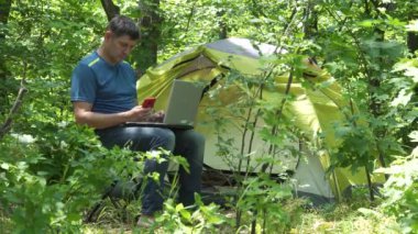 İşadamı ormandaki çadırın yakınındaki bir dizüstü bilgisayarın arkasında çalışıyor.