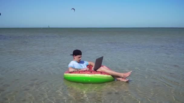 Een jonge zakenman werkt enthousiast achter een laptop zwaaiend op de golven van de zee — Stockvideo