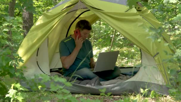 İşadamı ormanda bir çadırda dizüstü bilgisayarın arkasında çalışıyor. — Stok video