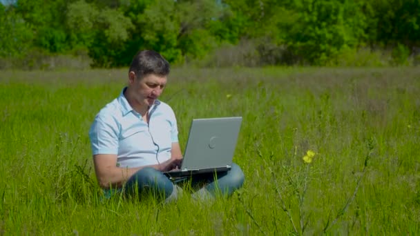 Homme d'affaires travaille derrière un ordinateur portable assis sur l'herbe — Video