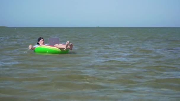 Un joven hombre de negocios está trabajando con entusiasmo detrás de un ordenador portátil balanceándose en las olas del mar — Vídeos de Stock