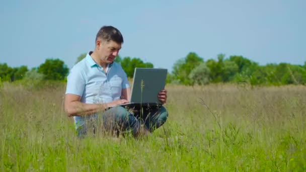 Empresario trabaja detrás de un ordenador portátil sentado en la hierba — Vídeo de stock