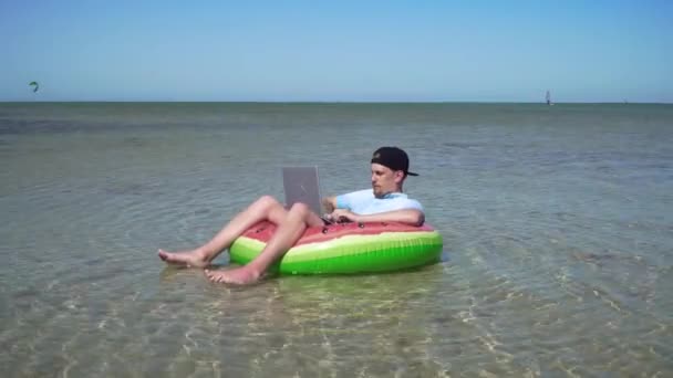 Een jonge zakenman werkt enthousiast achter een laptop zwaaiend op de golven van de zee — Stockvideo