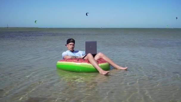 Genç bir iş adamı deniz dalgalarında sallanan bir dizüstü bilgisayarın arkasında hevesle çalışıyor. — Stok video
