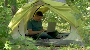 Ormandaki bir çadırda dizüstü bilgisayarla eğlenceli bir serbest yazar.