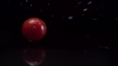 Kiraz domatesleri yavaş çekimde suya düşüyor ve siyah bir zemin var.