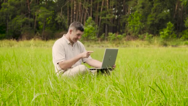 Usmívající se muž mluví na video on-line sedí na trávníku v trávě — Stock video