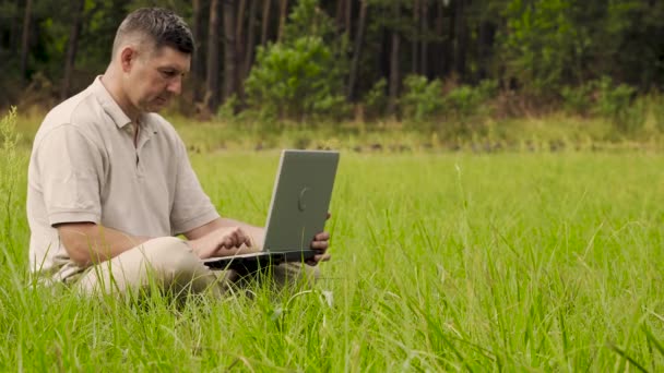 Empresário trabalha atrás de um laptop sentado na grama — Vídeo de Stock
