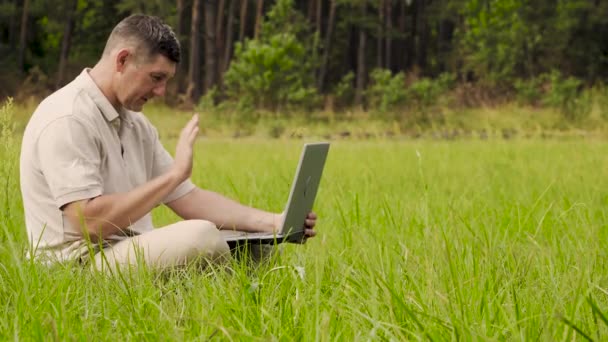 Homme souriant parler sur la vidéo en ligne assis sur la pelouse dans l'herbe — Video