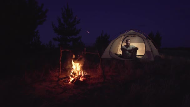 Een man rust in een tent bij een vuur. — Stockvideo