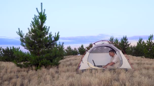 Мужчина использует ноутбук для общения на видео онлайн в палатке — стоковое видео