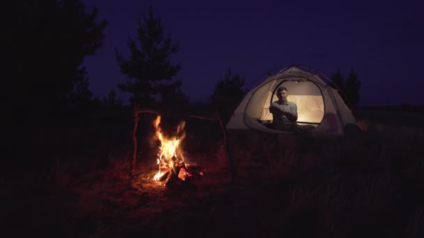 Мужчина лежит в палатке у костра — стоковое видео