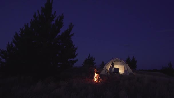 Freelancer Works behind a Laptopin in a tent near a fire — Stock Video