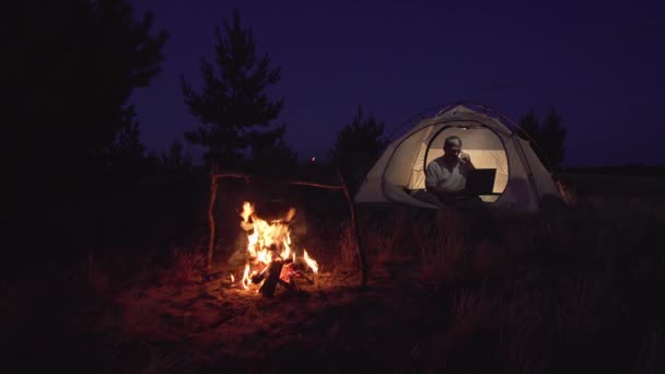 Freelancer Lavora dietro un computer portatile in una tenda vicino a un incendio — Video Stock