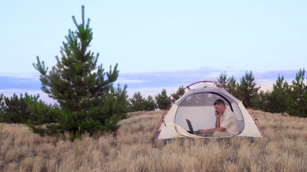 A man uses a laptop for talking on video online in the tent — Stock Video