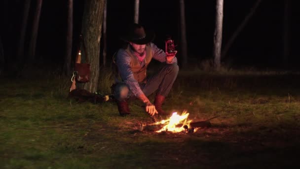 Ковбой зажигает керосиновую лампу в лесу ночью — стоковое видео