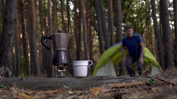 Café aromatique est préparé dans une cafetière geyser et un homme près d'une tente dans la forêt. — Video