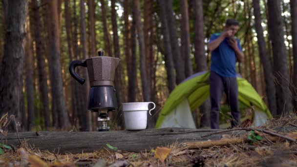 Ароматический кофе готовится в гейзере кофеварка и человек ест завтрак возле палатки в лесу. — стоковое видео