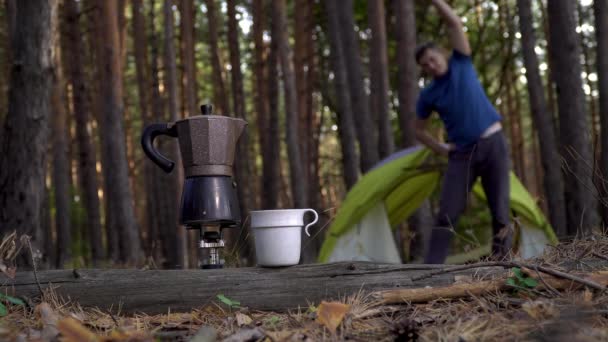 Le café est préparé dans une cafetière. Un homme fait de la gymnastique matinale près d'une tente dans les bois — Video