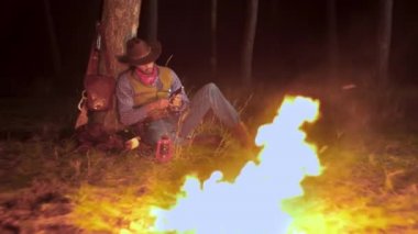 Geceleri ateşin yanında, ormanda bir kovboy.