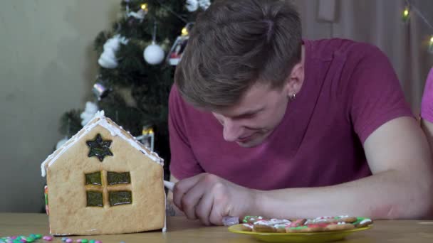 Um cara decora uma casa de gengibre de Natal — Vídeo de Stock