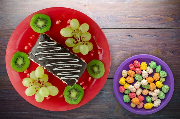 tatlı kek ve meyve (üzüm, kivi, nar) ahşap arka plan üzerinde. tatlı bir plaka Üstten Görünüm