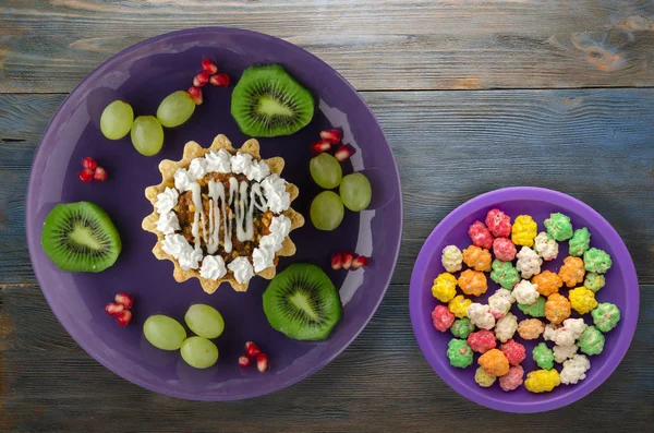 tatlı kek ve meyve (üzüm, kivi, nar) ahşap arka plan üzerinde. tatlı bir plaka Üstten Görünüm