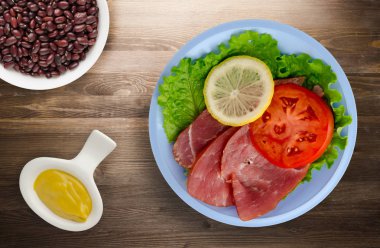 jambon salatası, domates ve limon bir plaka üzerinde. jambon bir ahşap arka plan .ham Üstten Görünüm