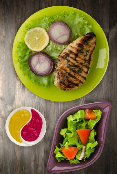 grilled chicken fillet with vegetables (lemon, salad, onion) on a wooden background. chicken fillet grilled on a plate top view
