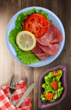 jambon salatası, domates ve limon bir plaka üzerinde. jambon bir ahşap arka plan .ham Üstten Görünüm