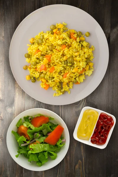 Asian healthy food. Rice (yellow) on a plate with vegetables. Eastern food on a wooden background.
