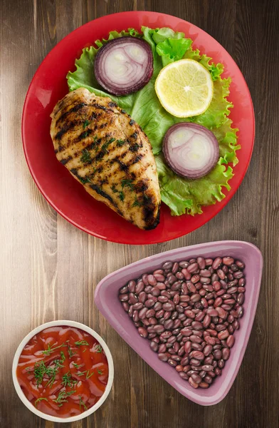 grilled chicken fillet with vegetables (lemon, salad, onion) on a wooden background. chicken fillet grilled on a plate top view