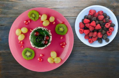 tatlı kek ve meyve (üzüm, kivi, nar) ahşap arka plan üzerinde. tatlı bir plaka Üstten Görünüm