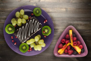 tatlı kek ve meyve (üzüm, kivi, nar) ahşap arka plan üzerinde. tatlı bir plaka Üstten Görünüm