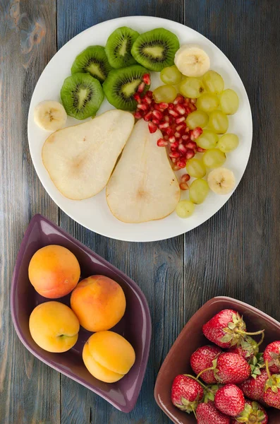 fruit mix (pear, kiwi, grapes, banana, pomegranate) on a wooden background. fruit on a plate