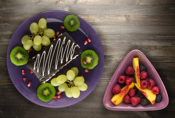 tatlı kek ve meyve (üzüm, kivi, nar) ahşap arka plan üzerinde. tatlı bir plaka Üstten Görünüm