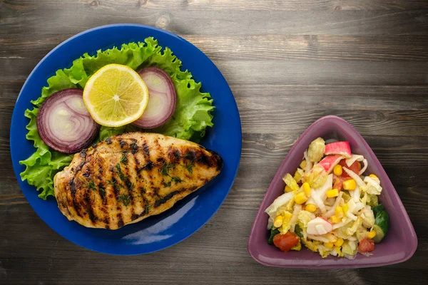 grilled chicken fillet with vegetables (lemon, salad, onion) on a wooden background. chicken fillet grilled on a plate top view
