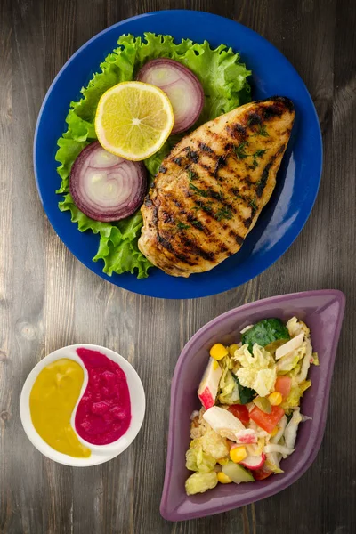 grilled chicken fillet with vegetables (lemon, salad, onion) on a wooden background. chicken fillet grilled on a plate top view