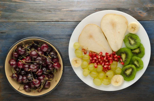 fruit mix pear, kiwi, grapes, banana, pomegranate on a wooden background