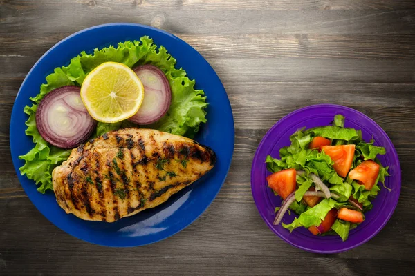 grilled chicken fillet with vegetables (lemon, salad, onion) on a wooden background. chicken fillet grilled on a plate
