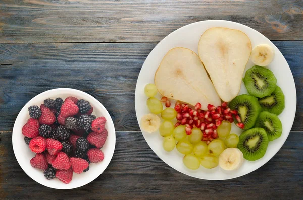 fruit mix (pear, kiwi, grapes, banana, pomegranate) on a wooden background