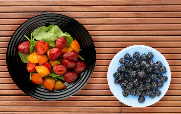 Comida vegetariana. comida saludable. una ensalada de espinacas, albaricoque, fresa en un plato sobre un fondo de madera — Foto de Stock