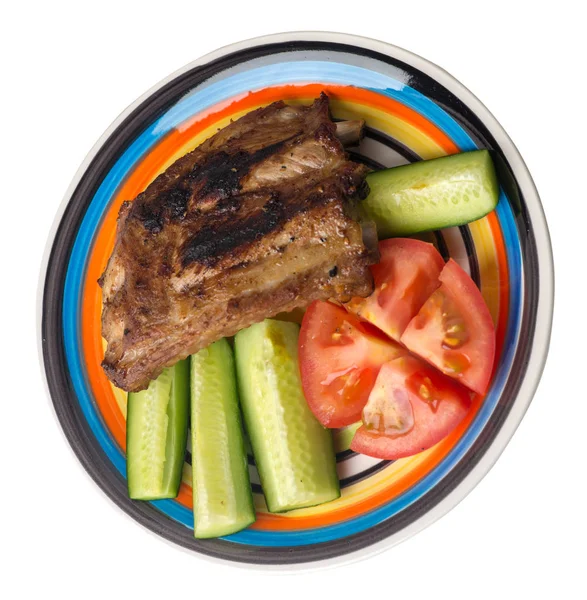 grilled pork ribs with sliced cucumbers and tomatoes on a plate. pork ribs isolated on white background.