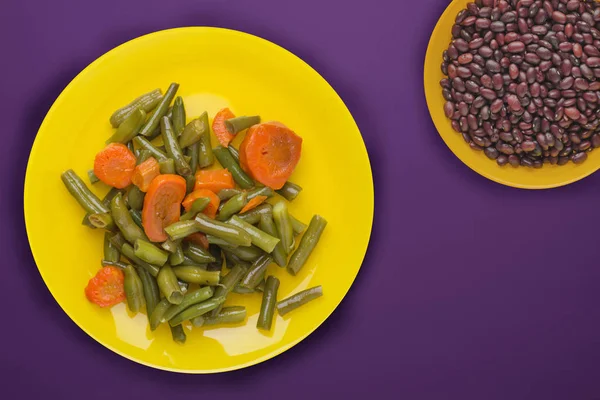 Green beans with garlic carrots on a yellow plate on a purple ba — 图库照片