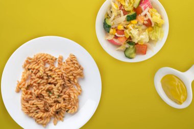 Domates soslu beyaz tabakta makarna ve sebze salatası.